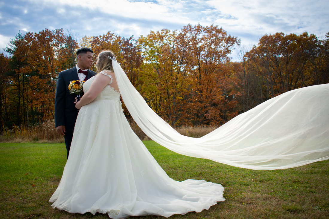 Bride and Groom in field with veil blowing in the wind