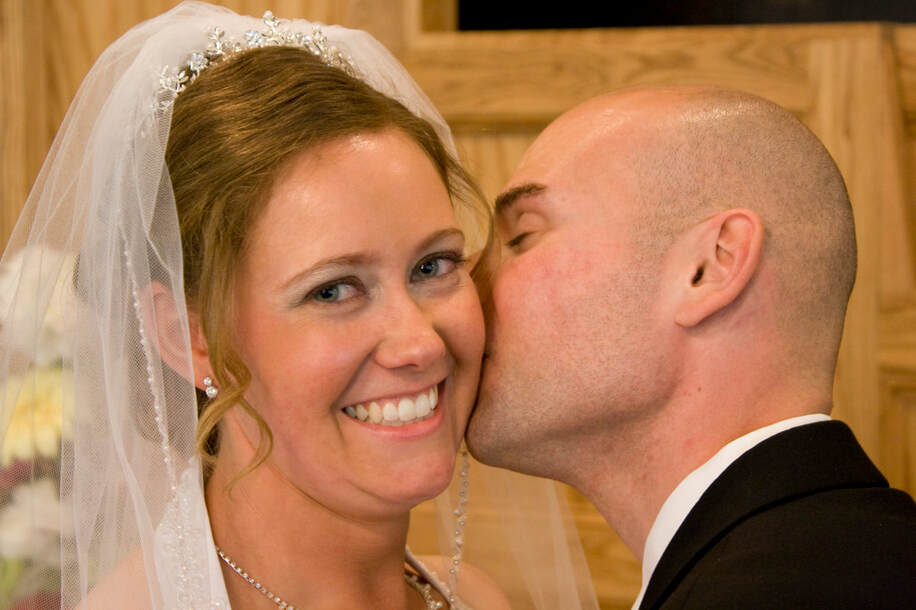 Bride smiling while groom kisses her on the cheek